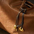 Brown leather bag with gold prayer wheel and cylindrical charms, featuring "Songmont" embossed on leather ties.