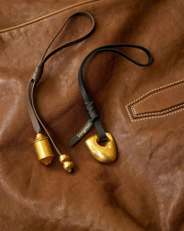 Gold prayer wheel charm with "Songmont" logo on a brown leather background.