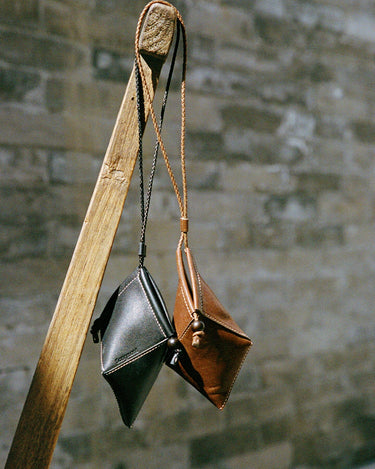 Prism Airpods Case in onyx black and sandal brown leather, featuring braided straps and sandalwood beads.