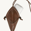 Brown leather Prism Airpods case with white stitching, braided strap, and wooden bead closure holding white AirPods case.