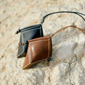 Songmont Prism Airpods Case in sandal brown and black leather with white stitching and wooden bead detail.