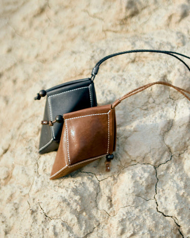 Songmont Prism Airpods Case in sandal brown and black leather with white stitching and wooden bead detail.
