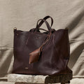 Deep brown pebbled leather tote bag with detachable pouch and 'Songmont' logo, displayed on rustic wood.