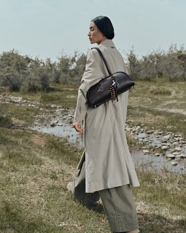 Prism Seed Charm in Onyx, a curved shoulder bag with beaded charms worn by a woman in a trench coat.