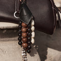 Prism Seed Charm featuring onyx and natural bodhi seeds on a dark leather bag.