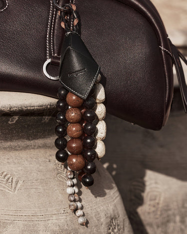 Prism Seed Charm featuring onyx and natural bodhi seeds on a dark leather bag.