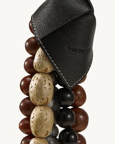 Prism Seed Charm in Onyx: black leather accent with embossed Songmont logo on a strand of mixed beads.