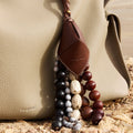 Prism Seed Charm with natural seeds and leather tag on a light beige Songmont bag