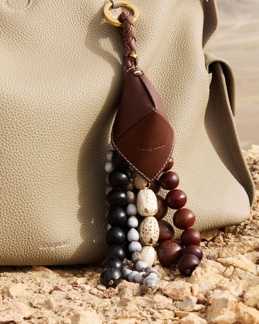 Prism Seed Charm with natural seeds and leather tag on a light beige Songmont bag