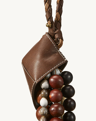 Brown leather pouch filled with mixed-color wooden and stone beads, attached to a braided strap.