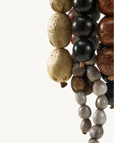 Prism Seed Charm accessory with diverse beads: textured light brown, smooth black, and marbled grey.