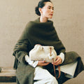 Woman in dark green wool coat holding amber shearling gather clutch set