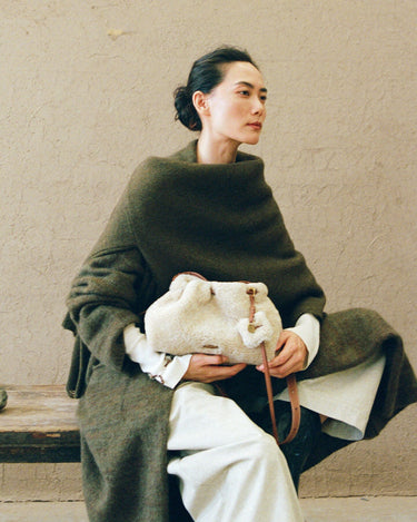 Woman in dark green wool coat holding amber shearling gather clutch set