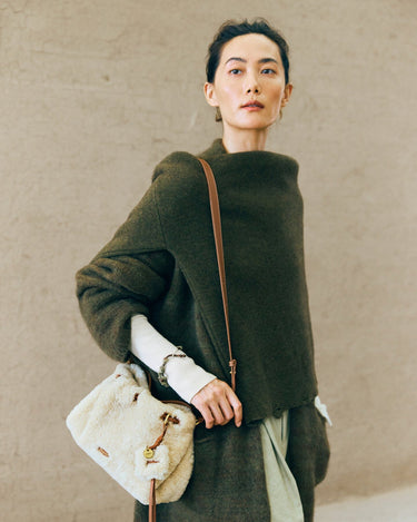 Amber shearling gather clutch set with leather strap, worn by a model in a green sweater.