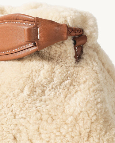 Amber shearling clutch with braided leather strap detail, showcasing cozy texture and stitching.