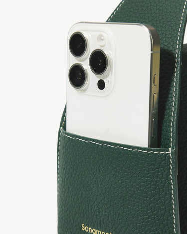 Green leather bag holds white iPhone Pro, showing camera and 'Songmont' logo.