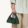 Small dark green pebbled leather drippy roof bag with white stitching and gold hardware, held by a person.