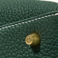 Green full-grain leather bag detail with stitched seam and 'song mont' engraved brass hardware.