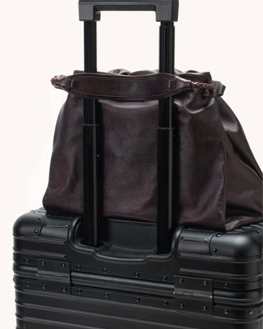 Dark brown leather Small Gather Bag Set draped over the handle of a black suitcase.