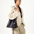 Woman holding an ebony leather Small Gather Bag Set with a drawstring closure and tassel detail.