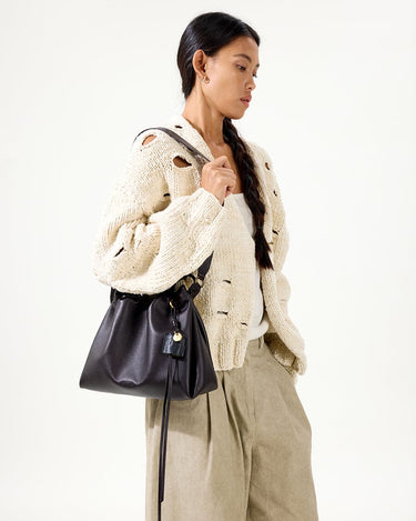 Woman holding an ebony leather Small Gather Bag Set with a drawstring closure and tassel detail.