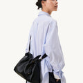 Small Gather Bag Set in Onyx black leather worn by a woman in a blue striped shirt.