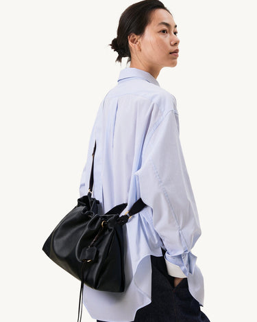 Small Gather Bag Set in Onyx black leather worn by a woman in a blue striped shirt.
