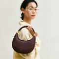 Small Luna Bag in burgundy full-grain leather with gold hardware, held by a woman wearing glasses.