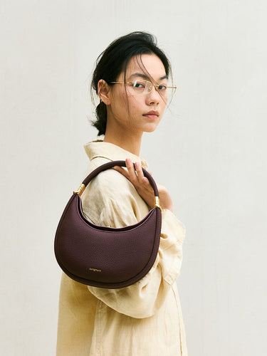 Small Luna Bag in burgundy full-grain leather with gold hardware, held by a woman wearing glasses.