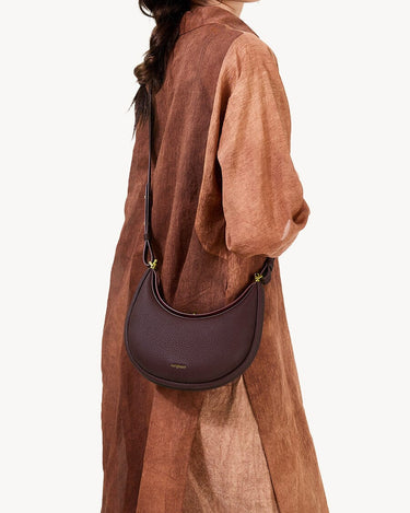 Burgundy textured leather Small Luna Bag worn crossbody with gold hardware.