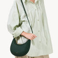 Small Luna Bag in emerald green pebbled leather, worn cross-body. Features curved silhouette and subtle embossed logo.