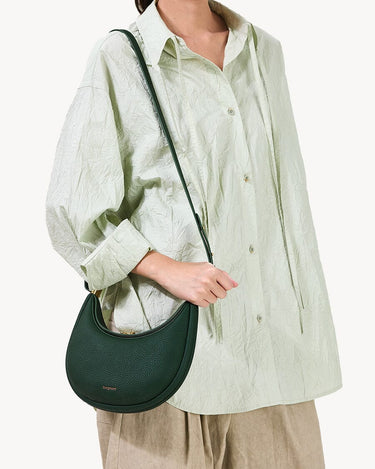 Small Luna Bag in emerald green pebbled leather, worn cross-body. Features curved silhouette and subtle embossed logo.