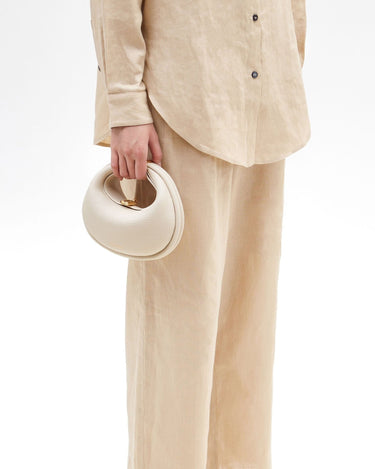 Small Luna Bag in ivory pebble-grain leather with gold hardware, worn by a person in cream linen attire.