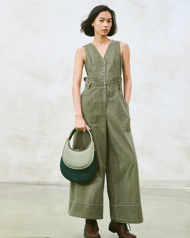 Small Luna Bag in Jade featuring dual-tone leather and gold hardware, held by a model in a green jumpsuit.
