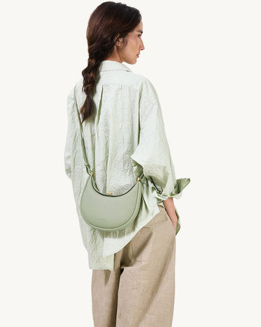 Small Luna Bag in jade green, crafted from full-grain leather with gold hardware, worn on the shoulder by a woman.