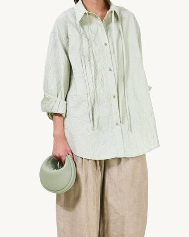 Jade pebble-grain Small Luna Bag with curved handle, paired with textured green shirt and beige pants.