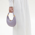 Small Luna Bag in lavender pebble grain leather with gold hardware, held by a person in white outfit.