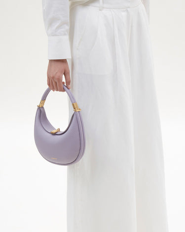 Small Luna Bag in lavender pebble grain leather with gold hardware, held by a person in white outfit.