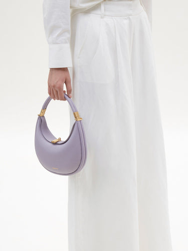 Small Luna Bag in lavender pebble grain leather with gold hardware, held by a person in white outfit.