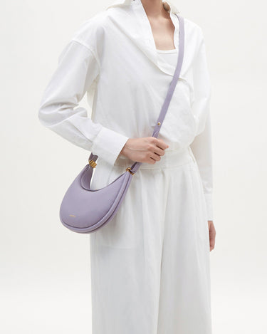 Small Luna Bag in lilac pebble leather with gold hardware, worn by a model.