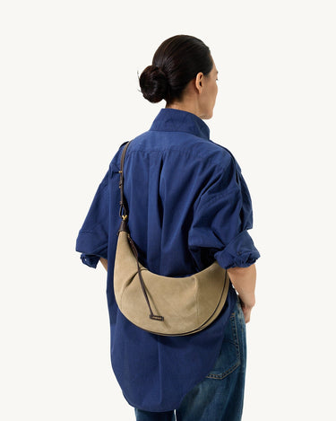 Medium Luna Hobo Bag in Dune Suede worn crossbody by a woman in a blue shirt and jeans.