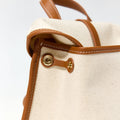 Close-up of the Small Shan Satchel Bag in Canvas, showing tan leather trim, stitching, and a gold snap closure with subtle embossed branding.