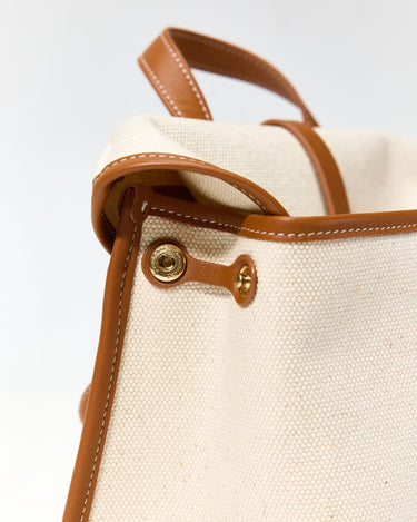 Close-up of the Small Shan Satchel Bag in Canvas, showing tan leather trim, stitching, and a gold snap closure with subtle embossed branding.