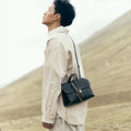 Onyx Small Shan Satchel Bag with leather tassel and gold hardware, worn crossbody outdoors.
