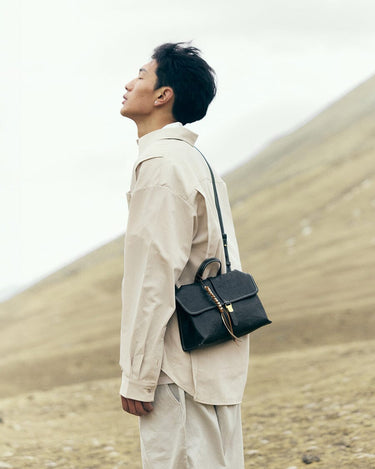 Onyx Small Shan Satchel Bag with leather tassel and gold hardware, worn crossbody outdoors.