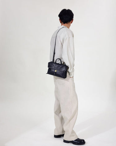 Small Shan Satchel Bag in Onyx: Textured vegetable-tanned leather, gold clasp, top handle, and adjustable strap.