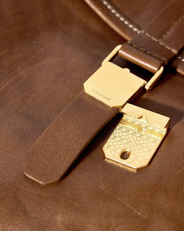 Brown leather Small Shan Satchel Bag with brass book clasp closure featuring intricate pattern and embossed Songmont logo.