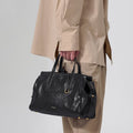 Small Yore Duffle Bag in onyx black vegetable-tanned leather with white stitching and gold hardware, held by a person.