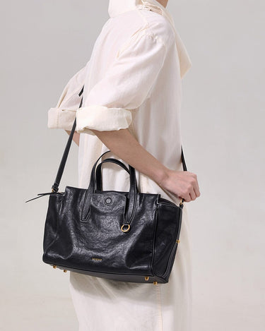 Small Yore Duffle Bag in Onyx: Vegetable-tanned leather travel bag with white stitching and gold hardware, worn by a woman.