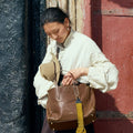 Small Yore Duffle Bag in Sandal brown leather with yellow tassel, carried by a woman.